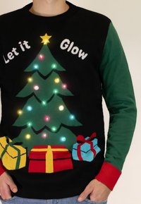 Schwarzer Pullover mit grünen Ärmeln; zeigt einen grünen Weihnachtsbaum mit bunten Lichtern, einem gelben Stern und Geschenken in Rot, Gelb und Blau.