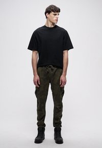 Fekete pamut rövid ujjú póló, zöld terepmintás cargo nadrággal, oldalzsebekkel, és fekete fűzős csizmával.