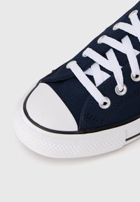 Navy canvas sneaker with white laces, rubber toe cap, and textured white sole. Features silver eyelets and a contrasting black trim.