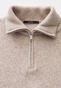 Beige soft knit sweater with a high collar and silver zipper half-closed, showing a black label with "someday." text.