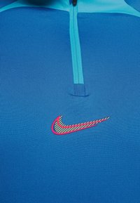 Sininen urheiluhaalari, jossa on puolivetoketju, sileä pinta ja monivärinen Nike-logo rinnassa.