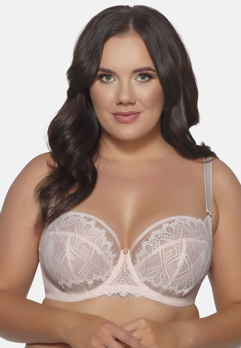 Reggiseno in pizzo rosa chiaro con pannelli trasparenti, coppe sagomate, cuciture decorative e un piccolo fiocco centrale. Spalline regolabili e supporto a ferretto.