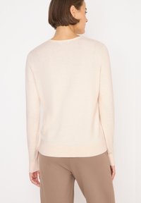Helles Pfirsichpullover aus weichem Strick, mit entspannter Passform, langen Ärmeln und Rundhalsausschnitt, kombiniert mit beigen Hosen.