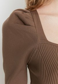 Braunter Strickoberteil mit enganliegendem Design, puffierten kurzen Ärmeln und vertikaler Rippstruktur entlang des Körpers. Sichtbares quadratisches Ausschnitt-Detail.