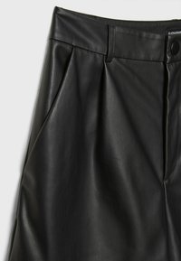 Pantalon taille haute en simili cuir noir avec passants de ceinture, poches latérales, plis devant et fermeture par bouton-pression.