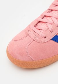 Rosa semskesneaker med teksturert overdel, med en blå aksentstripe og en gummirubber såle. Snøring med flate lisser.