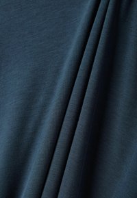 Dunkelblauer Stoff mit einer glatten, leicht strukturierten Oberfläche, der einen dezenten Glanz und fallende Falten aufweist und seine flexible Beschaffenheit zur Geltung bringt.