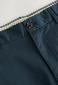 Un tissu bleu marine avec une texture lisse présente une fermeture à bouton et une doublure intérieure de couleur crème contrastante au niveau de la taille.