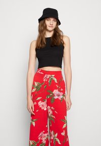 Top cropped preto combinado com calças largas florais vermelhas com padrões rosa e verde. Acessorizado com um chapéu preto tipo balde.