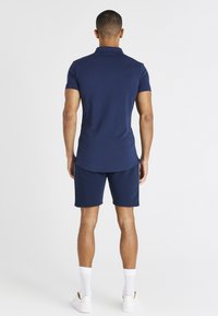 Laivansiniset lyhythihaiset poolopaidat, joissa on klassinen kaulus, yhdistettynä samanvärisiin shortseihin. Pehmeä rakenne ja urheilullinen istuvuus.