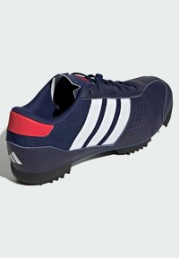 Merenkurkun urheilukengät, joissa on valkoiset kolme raitaa, verkkomateriaali yläosassa, kumipohja napeilla, ja punainen korostus kantapäässä.