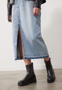 Blå denim midi skjørt med en frontslitt og slitt kant, kombinert med svarte lær ankelstøvler med tykk såle og glidelås på siden.