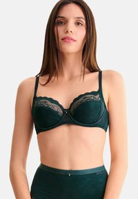 Donkergroene kanten bh met onderdraad, golfranden en een decoratieve centrale detail. Verstelbare bandjes en een bijpassende hoge taille slip.