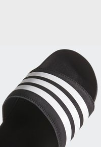 Sandalo scivoloso nero con una finitura testurizzata, caratterizzato da tre strisce orizzontali bianche sulla parte superiore. Design semplice, con apertura sulla punta.