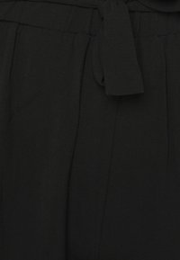 Pantalons noirs en tissu texturé, avec une taille nouée, des plis sur les côtés et une finition lisse. Pas de motifs visibles ni d'ornements.