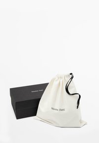 Baumwollzugbeutel in Creme mit schwarzem Kordelzug, neben einer mattschwarzen Box mit "Massimo Dutti" in weißem Text.