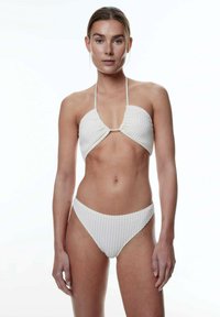 Weißer Bikini aus strukturiertem, honigwabähnlichem Stoff. Das Oberteil hat eine Bandeau-Form mit dünnen Bändern im Nacken und am Rücken, kombiniert mit minimal bedeckenden Unterteilen.