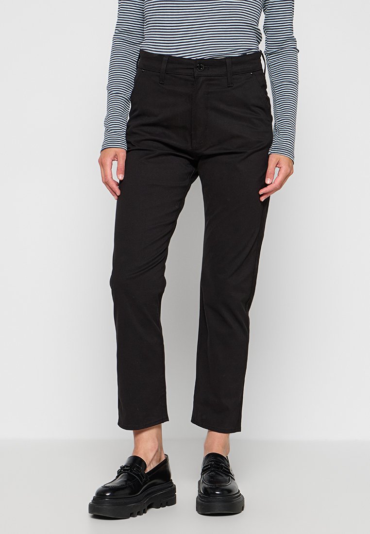 Pantalons noirs en tissu mélangé coton, avec une coupe ajustée, des passants de ceinture et une fermeture à bouton, associés à des chaussures noires épaisses.