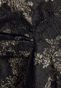 Tissu noir texturé avec des motifs floraux métalliques dorés et des coutures froncées créant des plis et de la profondeur dans le matériau.