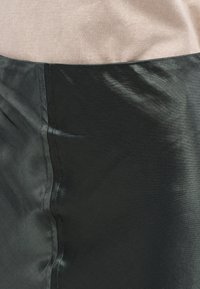 Μαύρο σατέν ύφασμα με λεία υφή, που διαθέτει διακριτική γυαλάδα. Η εικόνα εμφανίζει ραφές σε αντίθεση με το ανοιχτό μπεζ επάνω τμήμα.