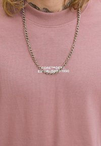 Kortærmet, lyserød crewneck t-shirt lavet af struktureret stof, parret med en sølvkæde med snoede led.