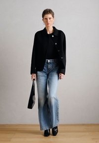 Blazer de lã preta com gola redonda, fecho de botões; top preto justo, jeans de cintura alta azul claro, sapatos pretos de bico fino, mala preta.