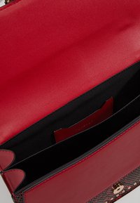 Bolso de mano de cuero rojo con un diseño elegante, que presenta un acabado suave, interior negro y un cierre en tono dorado, con un bolsillo interno.