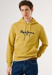 Yellow hoodie with a front pocket and drawstring hood, featuring "Pepe Jeans London" in navy. Worn over blue jeans, soft fabric.