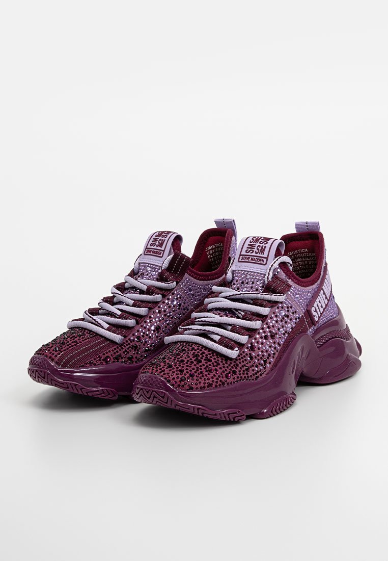 Zapatillas deportivas moradas con superiores texturizados, acentos brillantes y cordones en contraste de color lavanda. Presenta una suela gruesa con un patrón en zigzag.