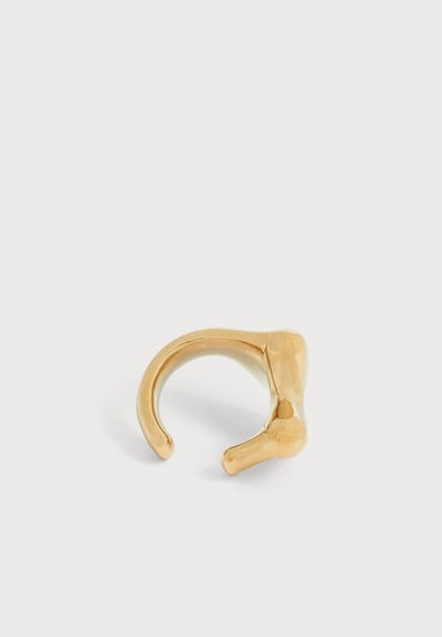Une bague manchette ouverte en or, à la forme irrégulière et sculpturale, présentée sur un fond uni clair.