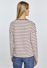 Striped long-sleeve shirt in cream with maroon stripes. Features a round neckline and relaxed fit. Fabric appears soft and lightweight.
