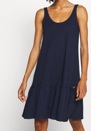 Sleeveless navy blue dress with scoop neck and ruffled hem worn by a woman with curly hair, shown from shoulders to knees.