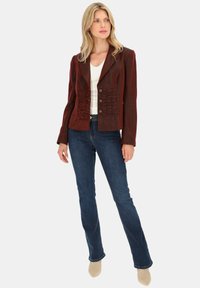 Czerwony żakiet o teksturowanej powierzchni z falbaniastymi akcentami i czterema guzikami, w zestawie z niebieskimi spodniami dzwonami i beżowym obuwiem. Prosta biała bluzka pod spodem.