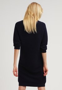 Abito a maglia a coste di colore blu navy con maniche lunghe, vestibilità rilassata e dettagli testurizzati sulla superficie. L'orlo e i polsini sono a coste per una maggiore struttura.