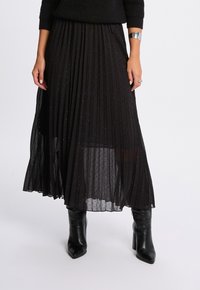 Sort plisseret nederdel med et gennemsigtigt overlay, prydet med små glimmer, lagdelt for tekstur, parret med sorte hælede støvler.