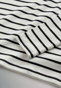 White ribbed fabric with alternating black stripes. Features a slightly rolled sleeve hem, with visible stitching along the edges.