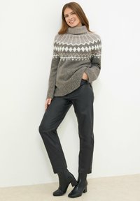 Maglione grigio a maglia con collettino alto e motivi geometrici bianchi, abbinato a pantaloni in ecopelle nera e stivali con tacco a blocco.