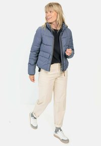 Lyseblå pufferjakke med tætsiddende design, lynlåslukning og sidelommer. Kombineret med beige bukser og sneakers, hvilket skaber et afslappet look.