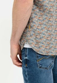 Korte mouwen, meerkleurig bloemenpatroon shirt gemaakt van lichte stof, gecombineerd met blauwe spijkerbroek met gele stitching.