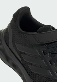 Chaussure de sport noire avec un dessus texturé, trois rayures en relief, un col rembourré et une semelle en caoutchouc avec des rainures marquées.