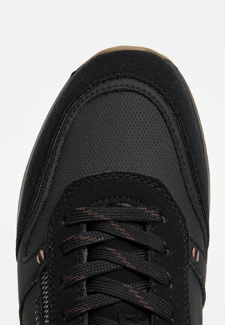 Baskets noires avec une surface texturée, en suède et en mesh, dotées de lacets sombres et d'accents cuivrés sur les côtés et les coutures.