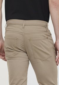 Pantalons khaki avec une texture lisse, poches arrière avec un rabat arrondi et passants de ceinture. Le tissu est léger avec une coupe ajustée.