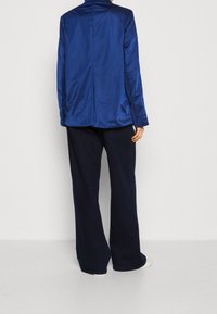 Sako z námořnicky modrého saténu s vysokým límcem a rovnou zadní švem, doplněné širokými námořnicky modrými kalhotami a bílými botami.