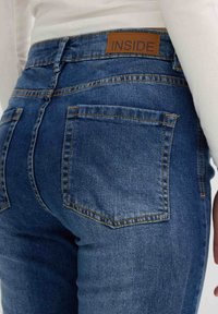 Jeans de denim azul marino con un diseño ajustado, que presentan una etiqueta de cuero marrón marcada como "INSIDE" y bolsillos traseros estándar. Costuras amarillas como acento.