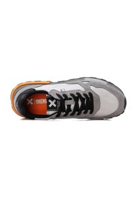 Zapatilla en tonos gris y blanco con cordones negros, detalles naranjas y una suela texturizada, que cuenta con un interior acolchado y una marca prominente en su interior.