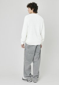 Un pull en tricot blanc avec une finition texturée, associé à un pantalon gris ample et des baskets noir et blanc, vu de dos.