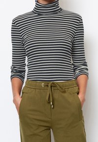 Stribet turtleneck i sort og hvid med lange ærmer, ribbet tekstur, sammen med olivengrønne trækstringsbukser med lommer.