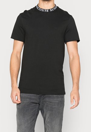 Czarna bawełniana koszulka z okrągłym dekoltem, z białym logo "Lacoste" oraz małym logo na piersi. Krótkie rękawy, luźny krój.