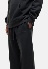 Zwarte hoodie met een voorzak en zwarte sweatpants met een gewatteerd logo. Soepele stof met een algemene relaxte pasvorm.