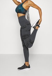 Un reggiseno sportivo con motivo leopardato turchese, leggings grigi a vita alta con camouflage e scarpe da ginnastica nere, che mostrano il design e la vestibilità dell'abbigliamento sportivo.
